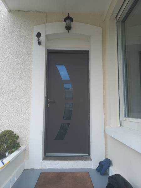 Installation d'une porte d'entrée moderne de couleur gris clair, avec parties vitrées en arc de cercle, à Octeville-sur-Mer